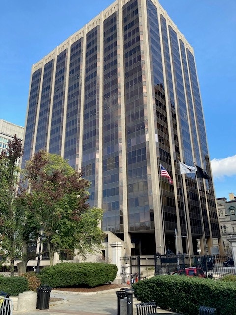 The American flag flies in front of a 22-story building with dark tinted windows. The McCormack Parking Garage was built at the base of the building.